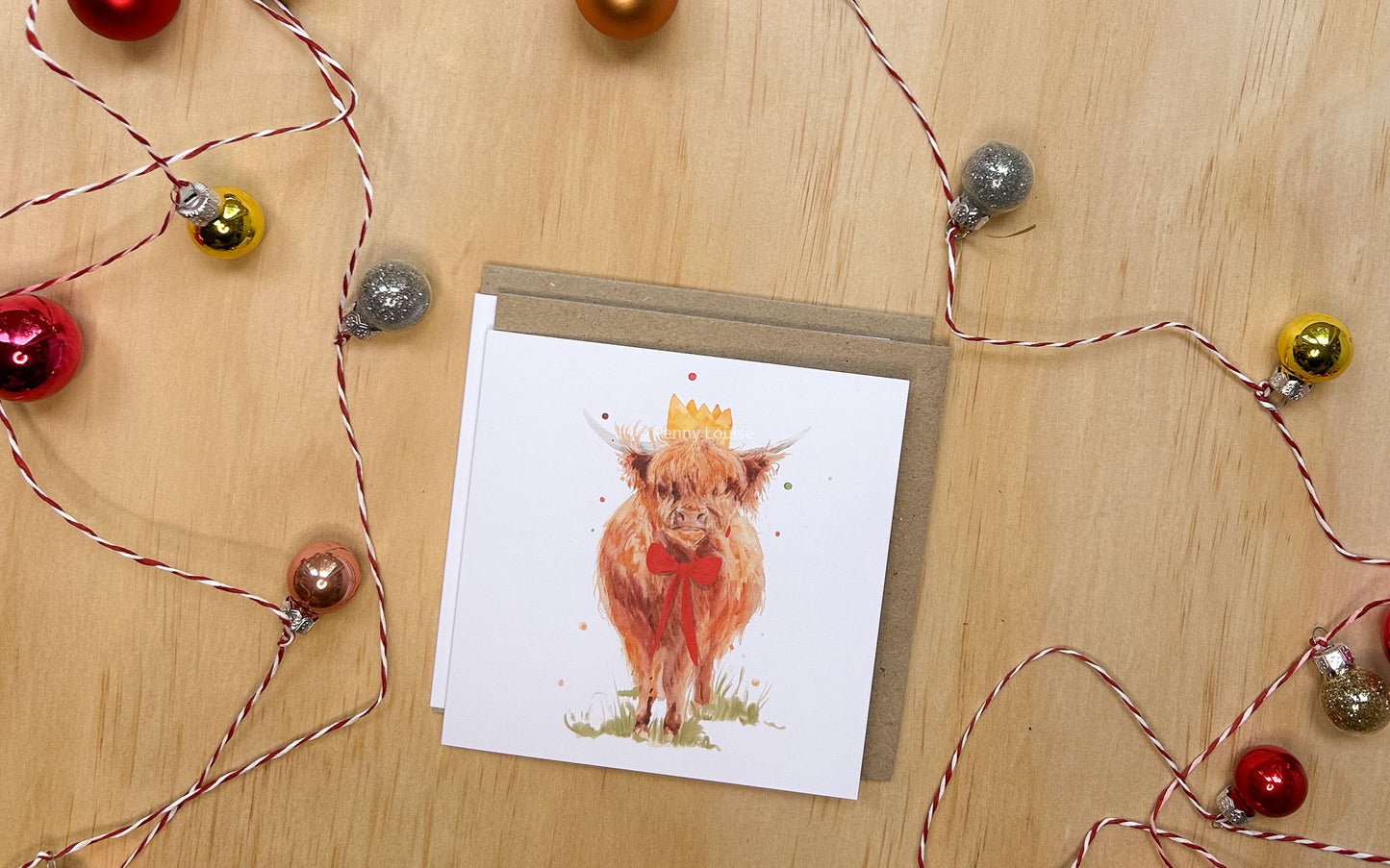 Card with a highland cow named Martha wearing a Santa hat on a wooden surface with string lights.