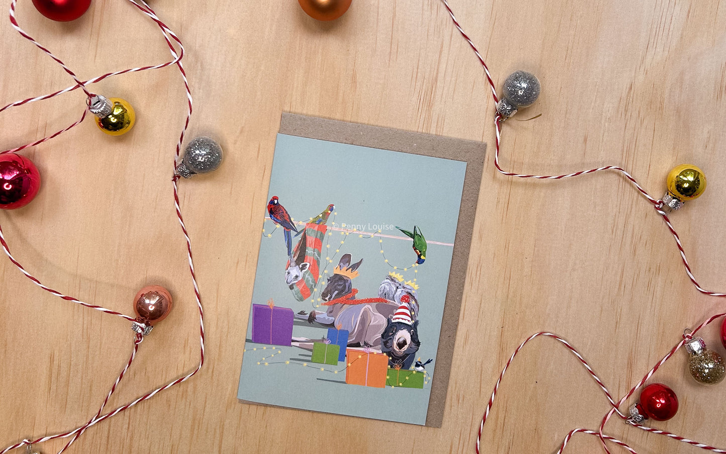 A greeting card with festive family Christmas celebration with unique charm of Australian wildlife starring Pappa kangaroo, joey, Rosella, Lorikeet, Tawny frogmouths, Wombat and a Blue Wren or course all decked out in holiday cheer. 