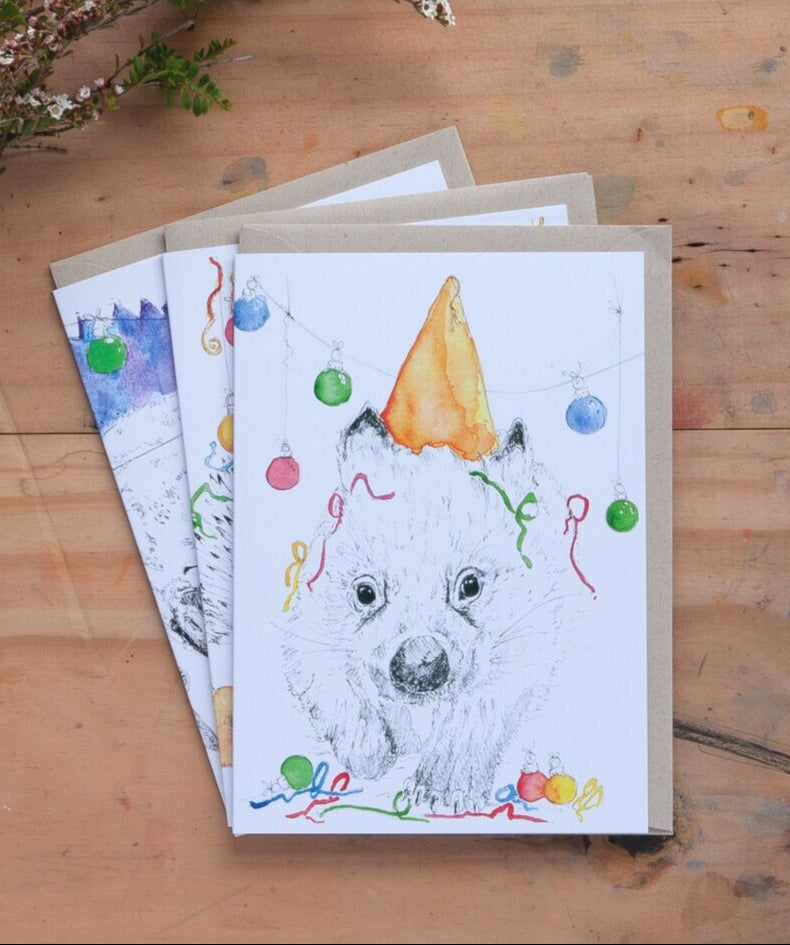 A greeting card with an illustration of a wombat wearing a party hat and Christmas baubles