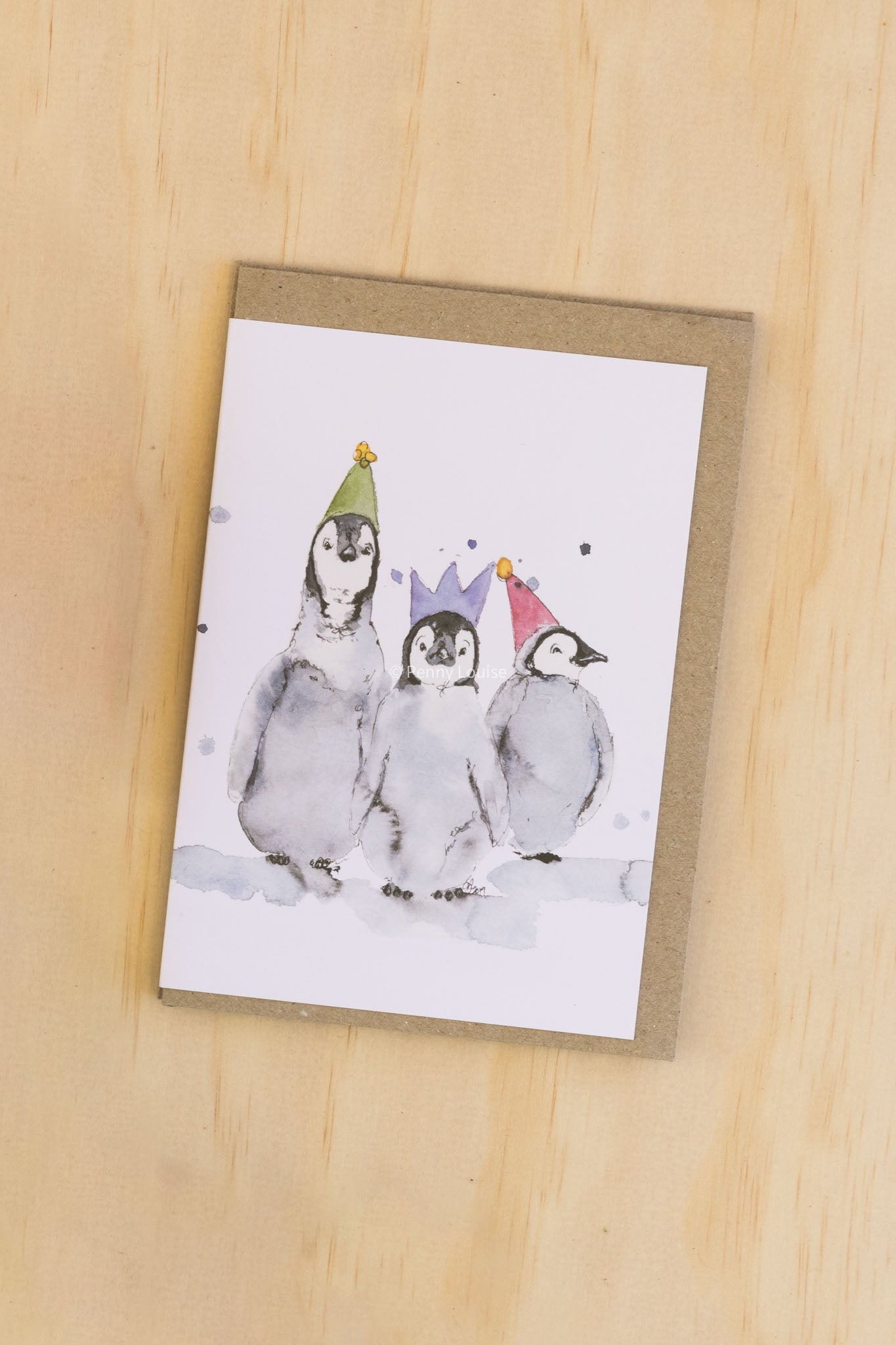 Card with penguin illustration wearing party hats on a wooden surface
