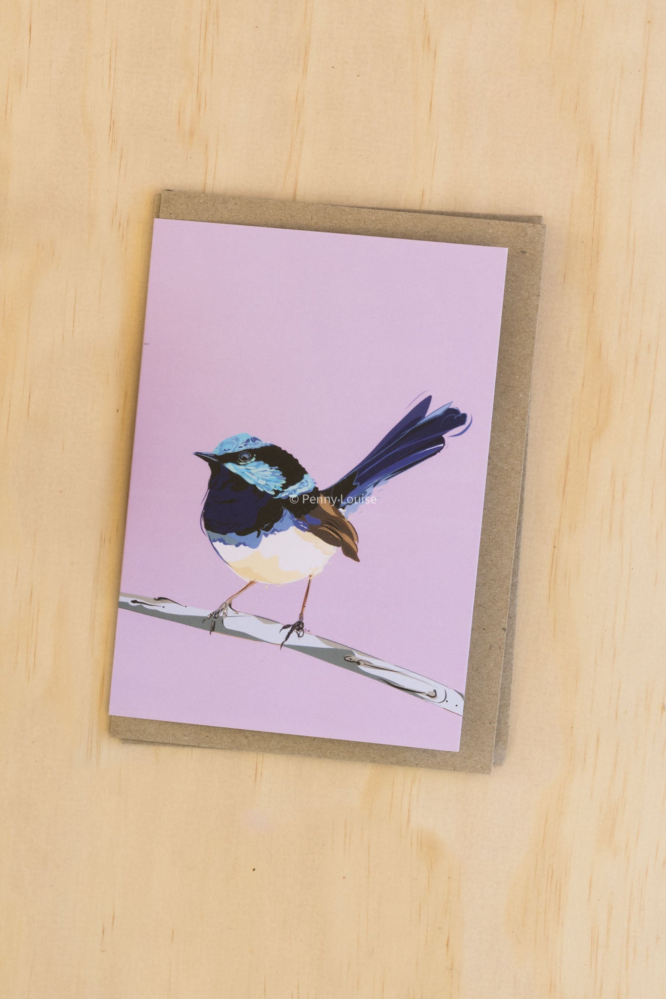 Greeting card with a bird illustration on a pink background, placed on a wooden surface.